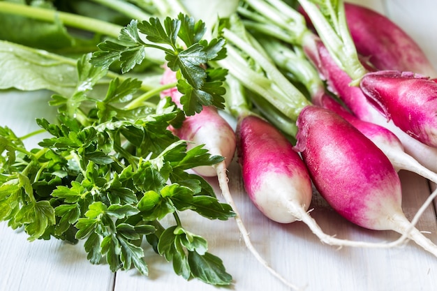 A bunch of fresh radish and herbs on a light wooden table.