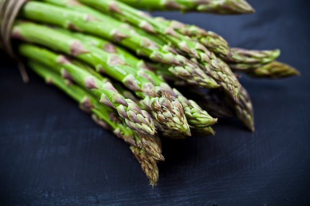 Bunch of fresh raw garden asparagus closeup on black board background. 