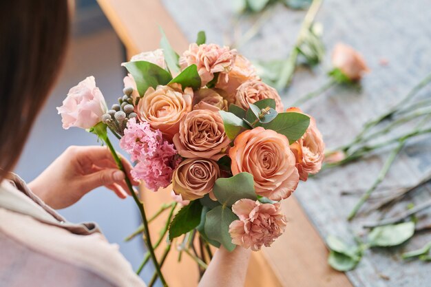 Mazzo di rose fresche e garofani di colori pastello tenuti da un giovane fiorista che produce mazzi di fiori sul posto di lavoro