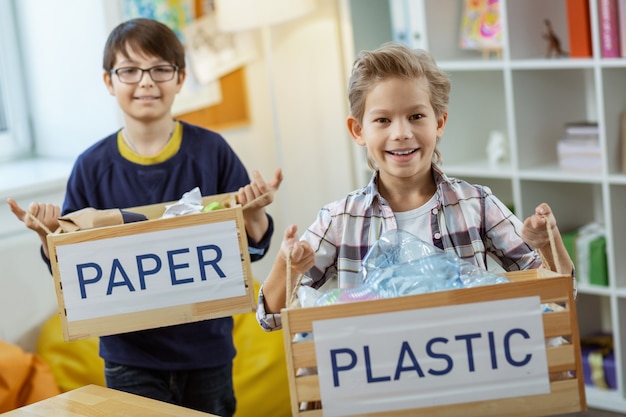 ゴミの束。分離されたプラスチックと紙の箱を持っている間、注意深い消費を示す幸せな勤勉な子供たち