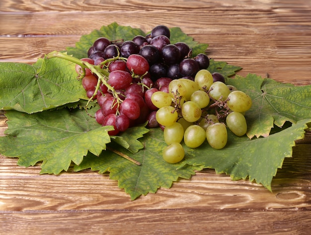 Bunch of grapes with green leaves on a wooden table 