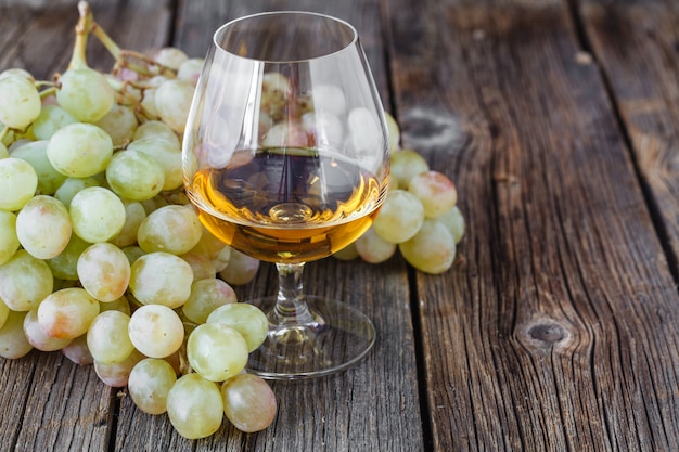 Bunch of grapes on wooden table with glass of cognac