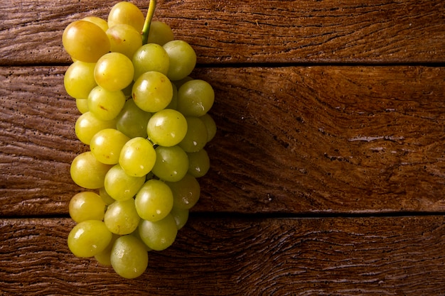 Bunch of green grapes, fruits of autumn, a symbol of abundance on rustic wood background.