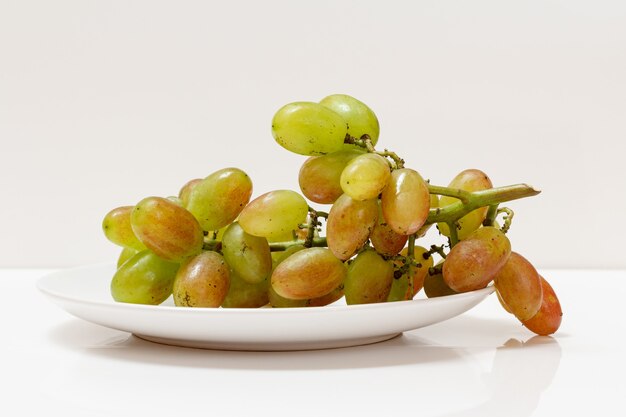 Bunch of green grapes on a plate with the white background.