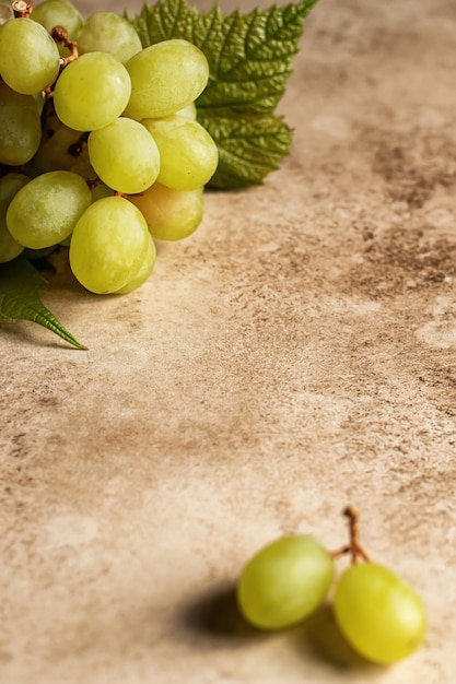 A bunch of green grapes with a leaf on brown textured background Text space