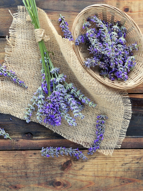 Bunch of lavender flowers on piece of fabric and basket on rustic wooden table