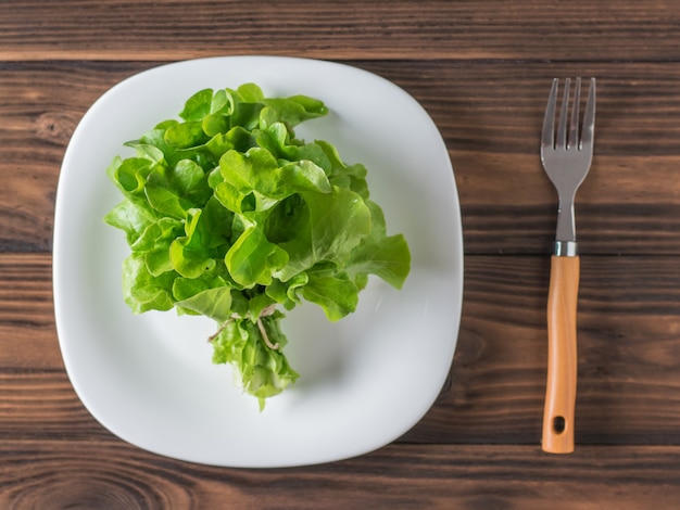 白い皿の上のレタスの束と木製のテーブルの上のフォーク。健康的な食事の概念。フラットレイ。