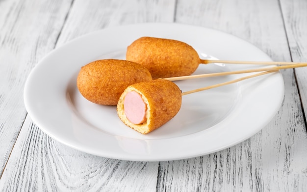 Bunch of mini corn dogs on white serving plate