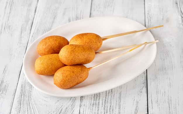 Bunch of mini corn dogs on white serving plate