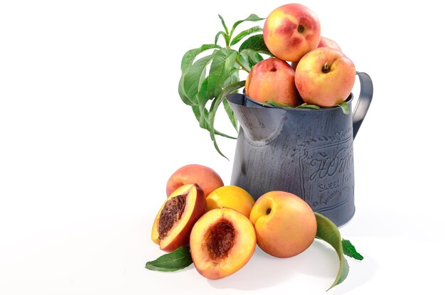 a bunch of peaches are in a blue pitcher with a leafy plant