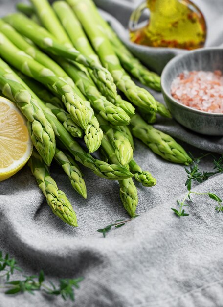 Bunch of raw asparagus stems with different spices on grey concrete background