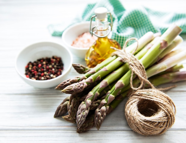 Bunch of raw asparagus stems with different spices and ingredients on wooden surface