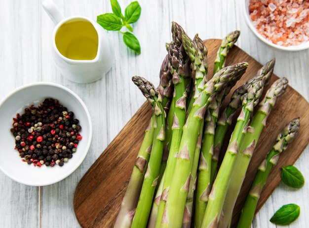 Bunch of raw asparagus stems with different spices and ingredients on wooden table. Top view, flat lay.