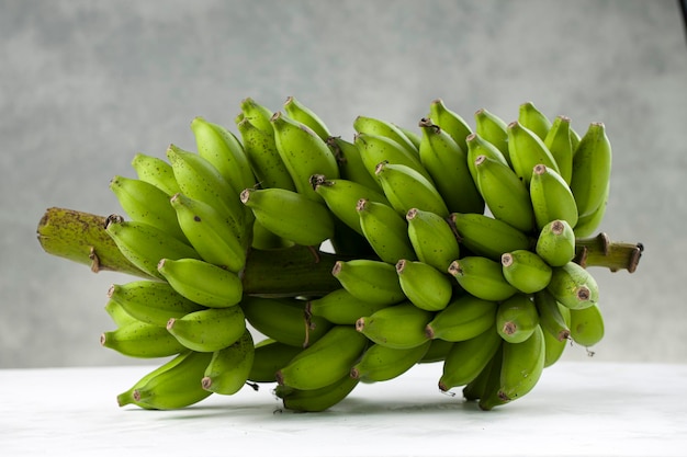 Bunch of raw banana or green banana placed on a white surface with grey textured background isolated