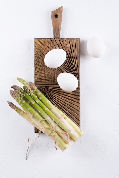 Bunch of raw fresh asparagus with eggs on a gray concrete background