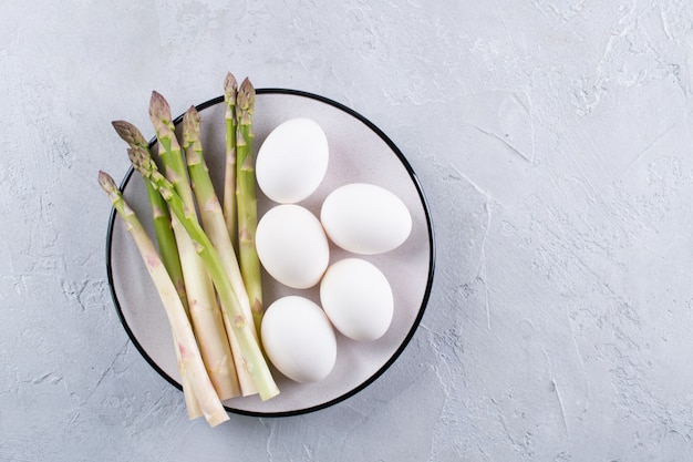 Bunch of raw fresh asparagus with eggs on a gray concrete background