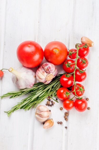 Bunch of red cherry tomatoes with green rosemary garlic and spices on white old table