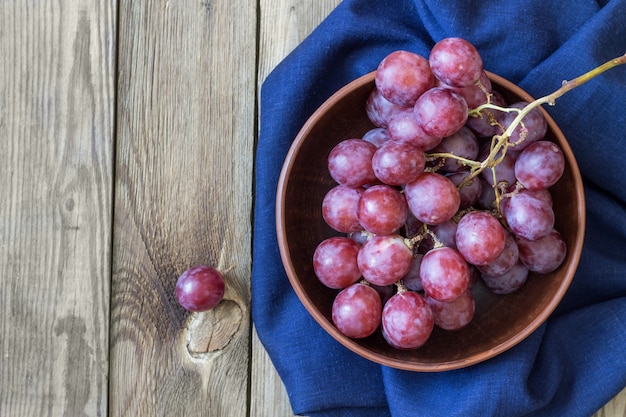 Bunch of red grapes on blue textiles in a bowl, on a wooden table. Copy space. Rustic style