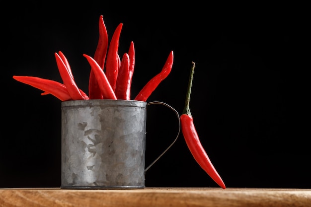 A bunch of red hot peppers in a metal cup on a black background. Culinary concept. Hot spice. Close-up.