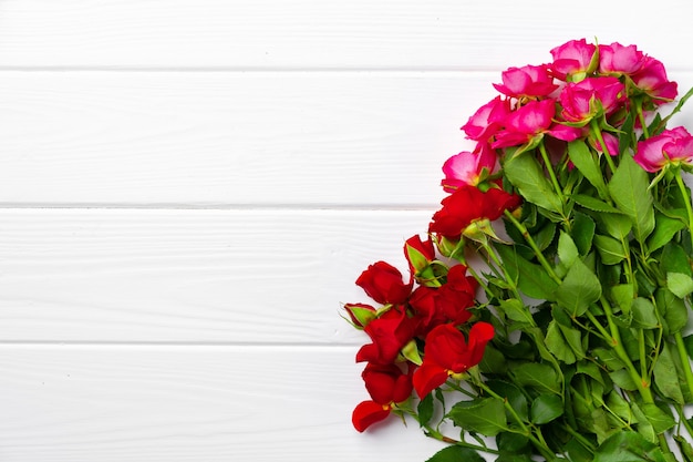 Букет из красных и розовых роз на белом деревянном фоне вид сверху