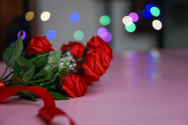a bunch of red roses tied with a red ribbon on a pink background and pink bokeh