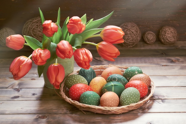 Bunch of red tulips Easter eggs in wattle tray Springtime decorations on rustic wooden background Retro toned image of Easter decorationsin low key Sunlight shadows