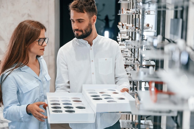 Bunch of replaceble lenses Man and woman in the glasses store Helping to choose product