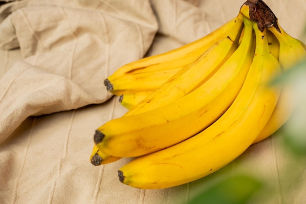 A bunch of ripe yellow bananas on a beige textile surface representing concepts of healthy eating an