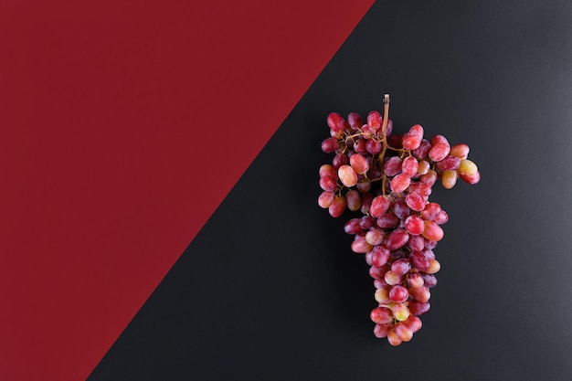 Bunch of rose grapes on a geometric double color wine red and black background, top view