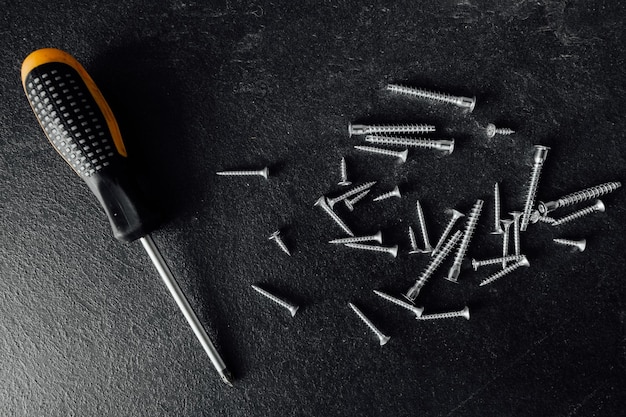 A bunch of self-tapping screws on the table. On a dark background.