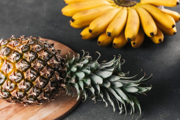 A bunch of small ripe bananas and pineapple on a dark gray rough background.