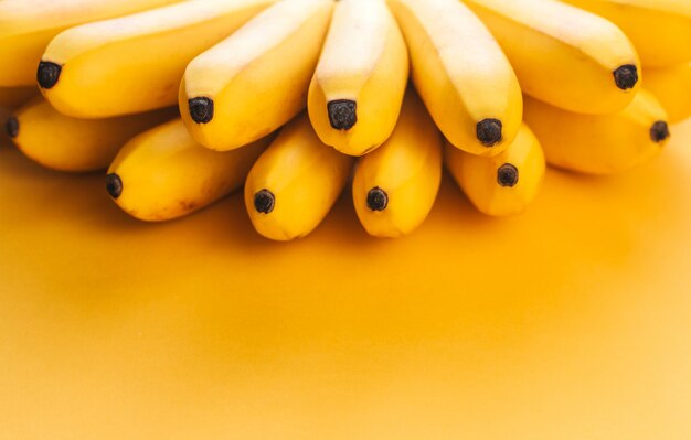 A bunch of small ripe bananas on a yellow background copy space