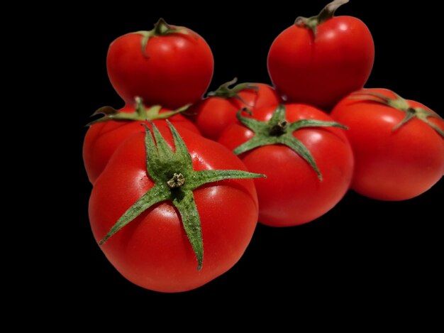 A bunch of tomatoes with green stems and green leaves isolated on black background