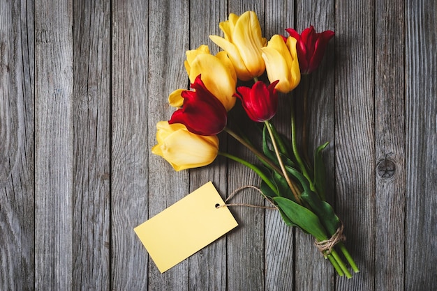 Bunch of tulip flowers with blank name card on wooden background copy space