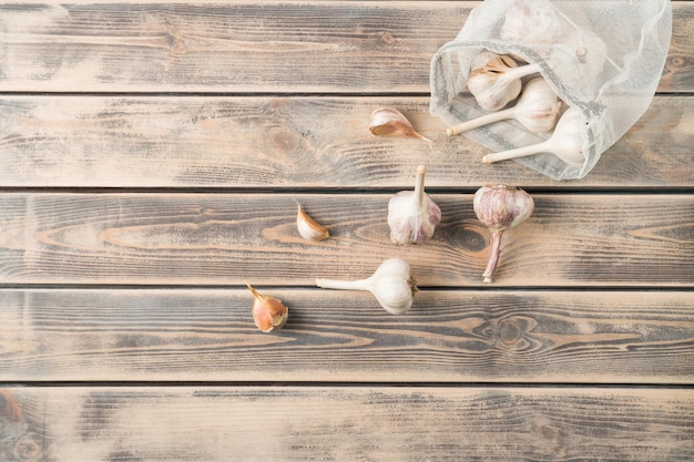 Bunch of unpeeled garlic on faded wooden table top view Eco fabric poach full of aromatic spice Food or healthy diet concept Separated location of garlic cloves Planking Culinary and cooking