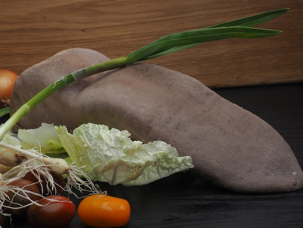 A bunch of vegetables on a table with a wooden board behind them