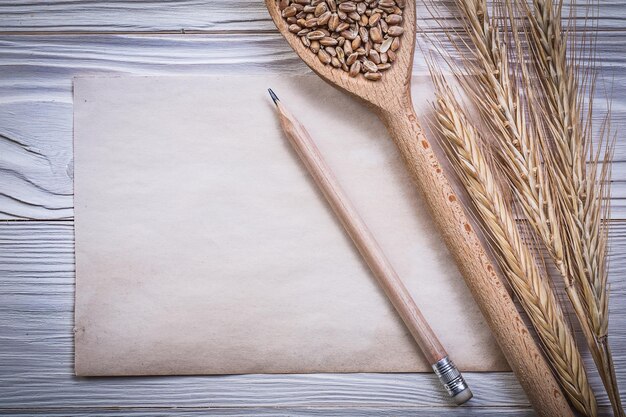 Bunch of wheatrye ears wooden spoon grain pencil vintage paper sheet on wood board