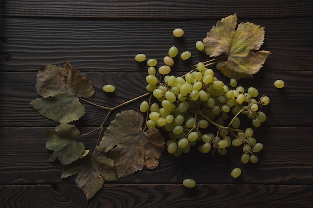 Bunch of white grapes, dry leaves on the dark wooden surface. Top view