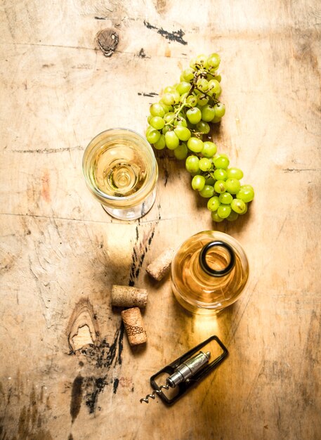 Bunch of white grapes with a bottle of wine, a corkscrew and stoppers. On wooden background.