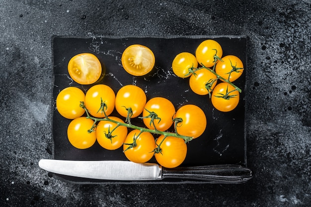 Bunch of  yellow cherry tomato on a marble board. Black table . Top view.