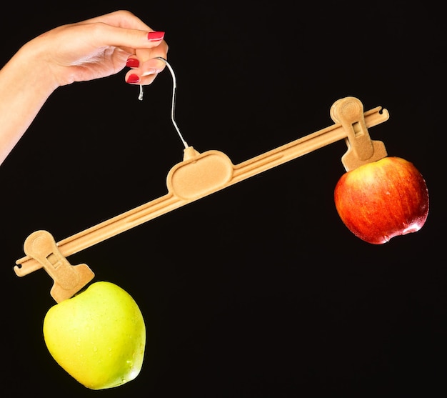 Bunches of green and red apples with unequal weight Female hand holds hanger with fruits on tips