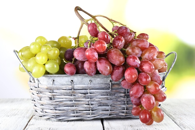 Bunches of ripe grape in wicker basket on wooden table on natural background