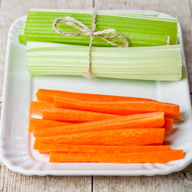 Bundle of fresh green celery stems and carrot in plate
