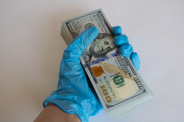 Bundle of one hundred dollar bills in hand in a medical glove on a white background