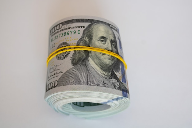 A bundle of one hundred dollar bills rolled up and tied with an elastic band on a white background