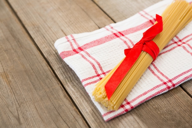 Bundle of raw spaghetti tied with red ribbon on napkin