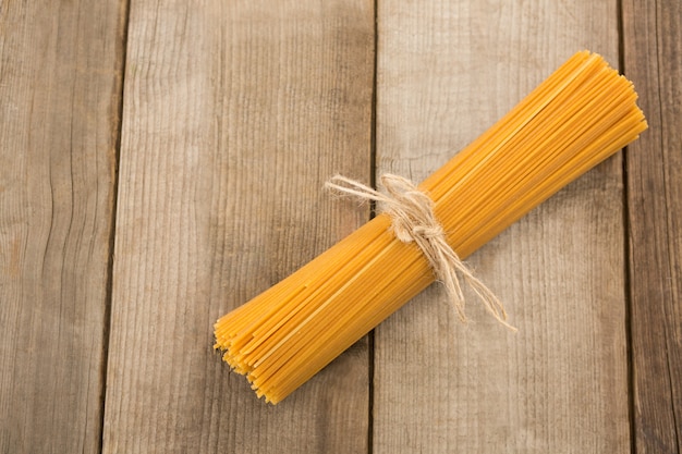 Bundle of raw spaghetti tied with rope on wooden surface