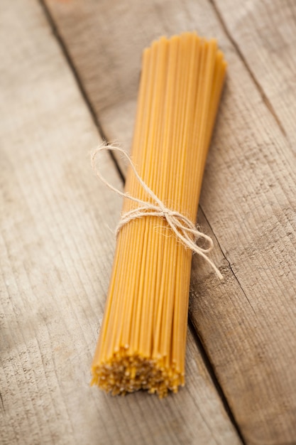 Bundle of raw spaghetti tied with white ribbon on wooden surface