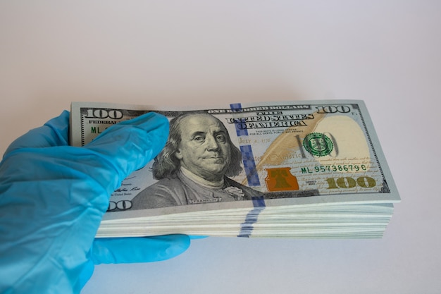 bundle of us hundred dollar bills in hand in blue glove