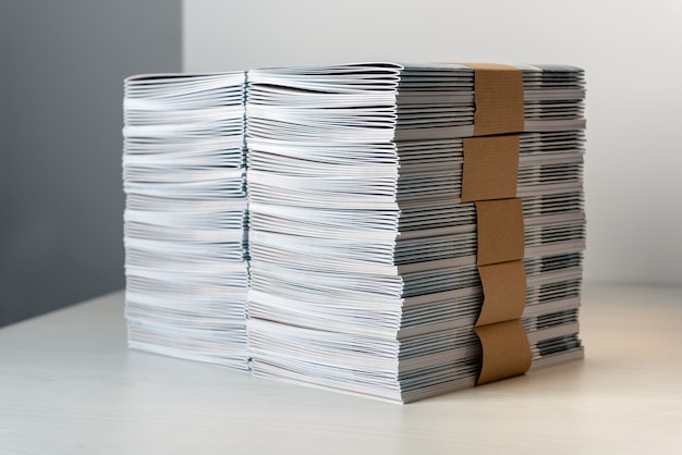 Bundles of newly printed catalogues fastened with brown paper arranged neatly in a stack on a white table